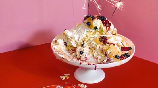 Partially eaten Pavlova Meringue Eton Mess, covered in persimmon jam, mixed berry compote, lemon curd, vegan lemon curd, whipped cream, fresh raspberries, fresh blueberries and zabaglione cream on cake stand. Photo by Charles Malene for MoodyEater™