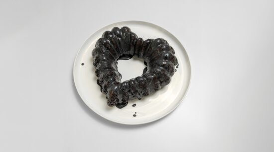 Jet Black Velvet Cocoa chocolate cake, in the shape of a heart, covered in black sugar glaze, on a white plate. Photo by Charles Malene for MoodyEater™